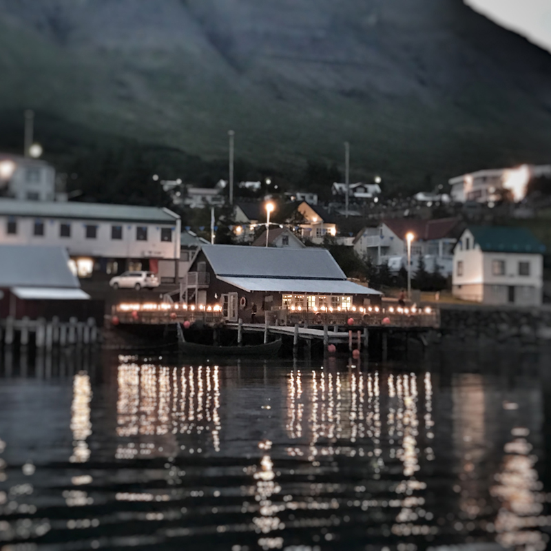 Upplýstur veitingastaðurinn speglast í firðinum í rökkri